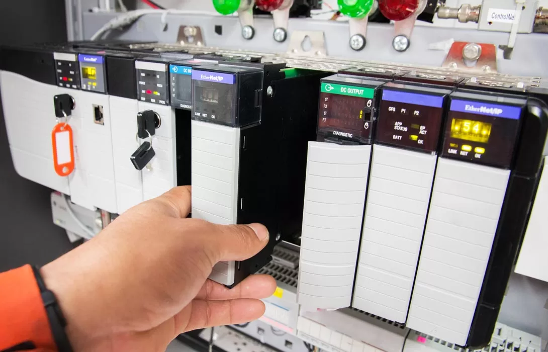 Foto com mão inserindo módulo no painel elétrico com sistema de automação CLP/PLC.